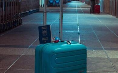 Ein blauer Koffer und ukrainischer Reisepass in einer leeren Flughafenhalle.