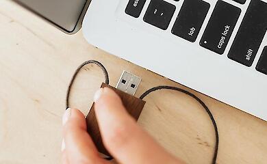 Eine Hand steckt ein USB-Gerät in den Anschluss eines geöffneten Laptops.