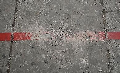 Eine rote Linie auf den Betonplatten eines Gehwegs, in der Mitte von Schritten abgelaufen
