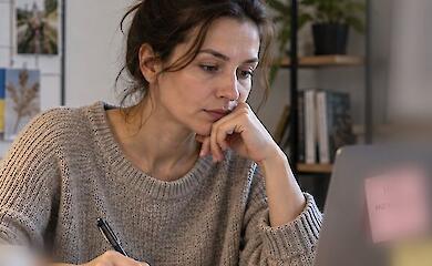 Eine Frau am Schreibtisch &uuml;berlegt ihre Jobsuche und schreibt einen Plan neben ihrem Laptop auf.
