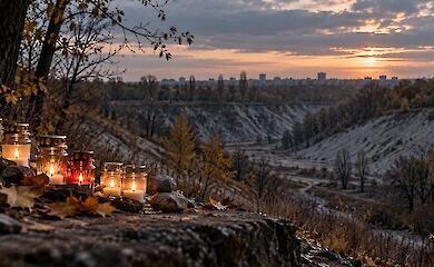 Gedenkkerzen und Steine vor einer herbstlichen Schlucht bei Sonnenuntergang.