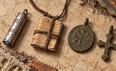 Metallplättchen, Papyrusbündel, rundes Medaillon und ein Kreuz auf Steinoberfläche.